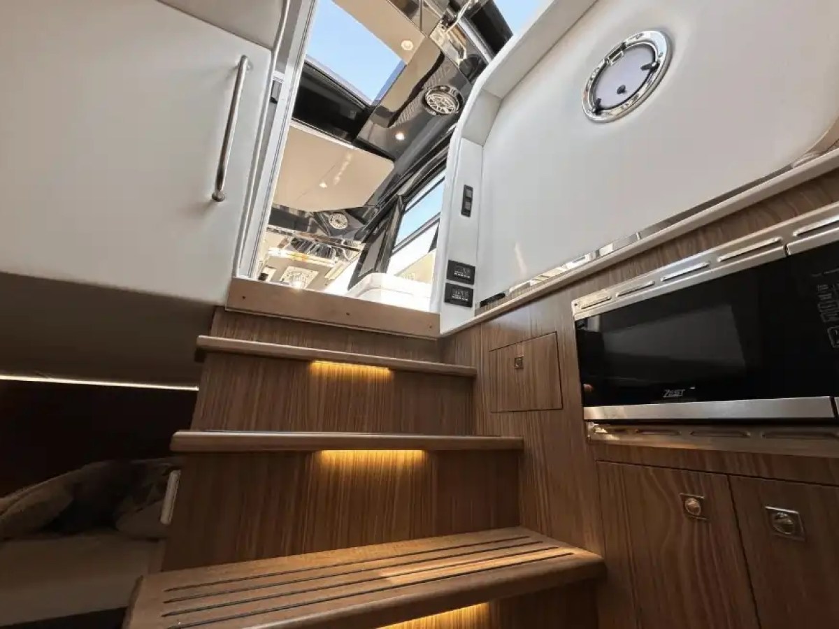 Wooden stairs in a yacht interior with overhead skylight and built-in microwave.