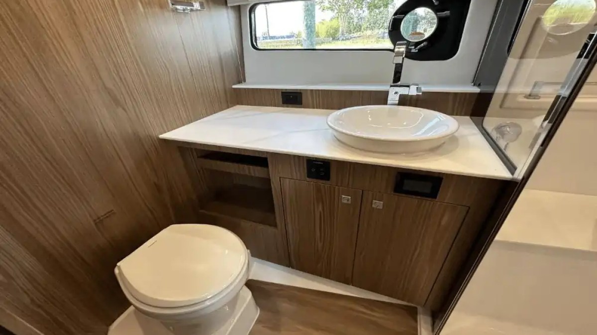Compact wooden bathroom with a round sink, faucet, and toilet, under a window.