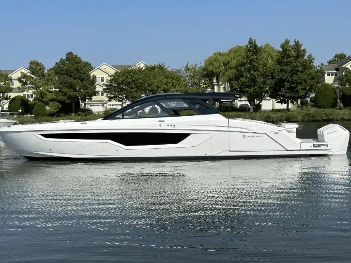 White motor yacht on calm water with trees and houses in the background.