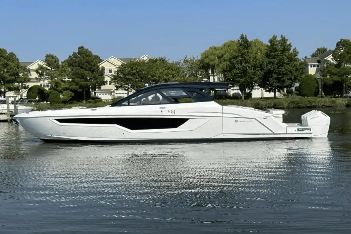 White motor yacht on calm water with trees and houses in the background.