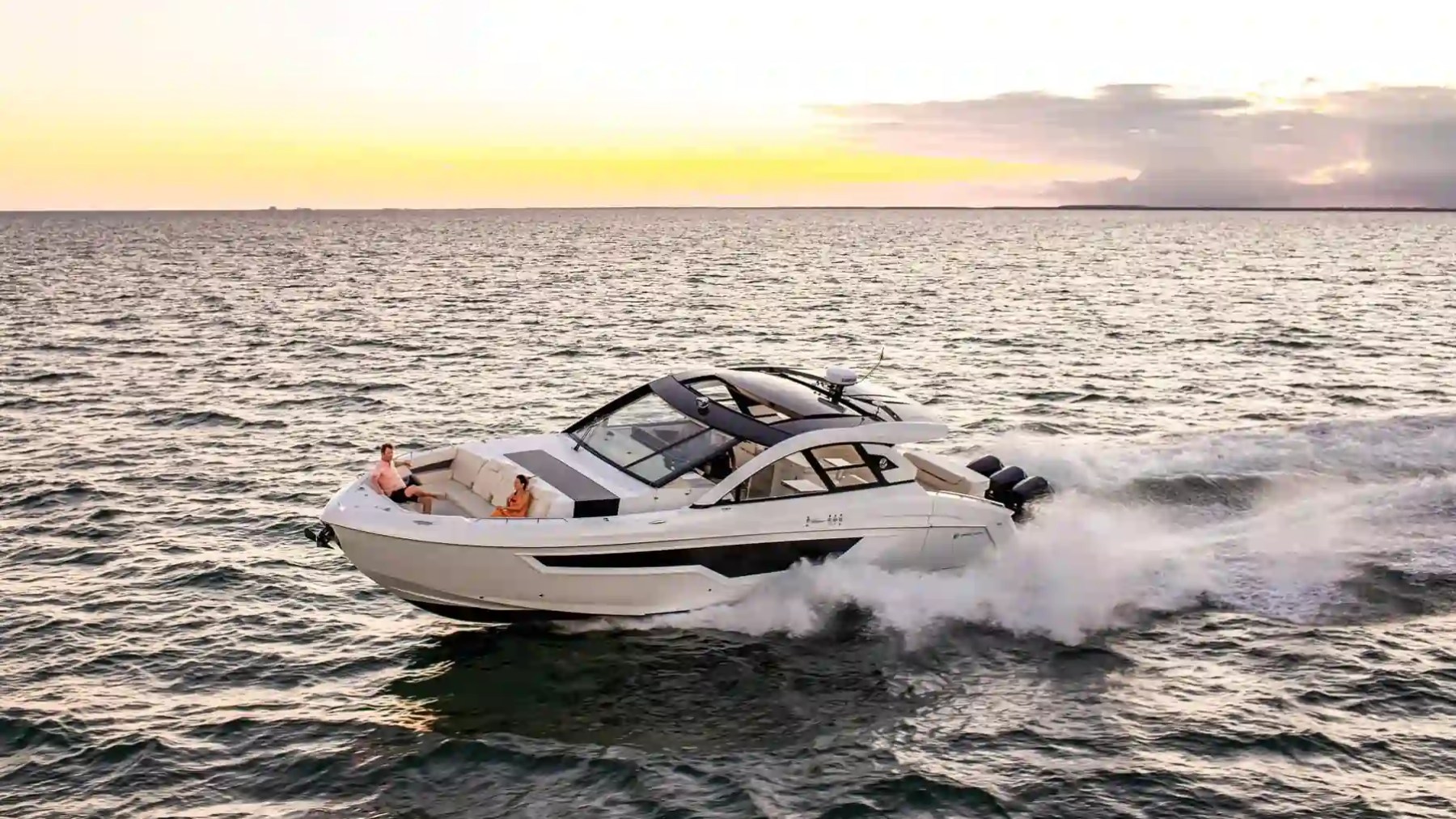 A speedboat cruising on the ocean during sunset with two people on deck.