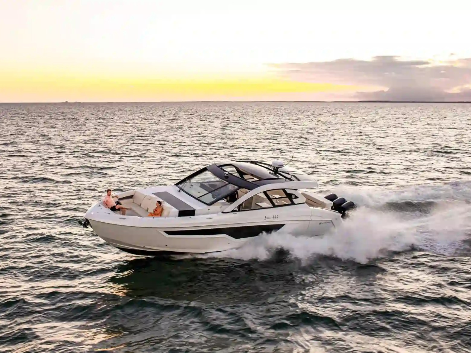 A speedboat cruising on the ocean during sunset with two people on deck.