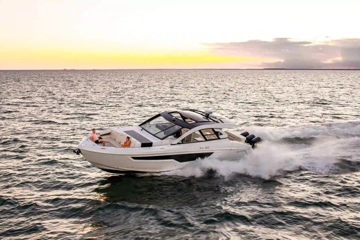 A speedboat cruising on the ocean during sunset with two people on deck.