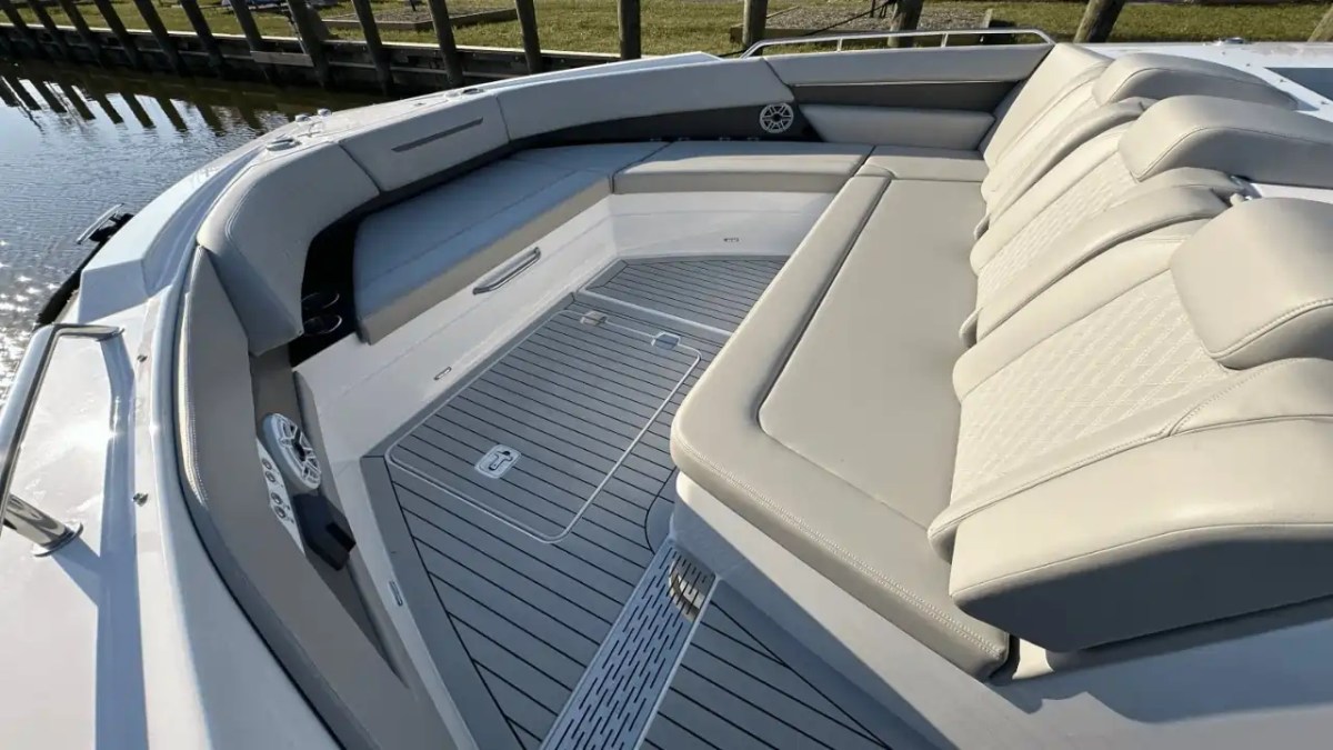 Boat's bow seating area with gray cushioned seats and speakers by the water.