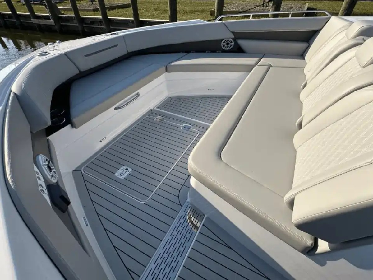Boat's bow seating area with gray cushioned seats and speakers by the water.
