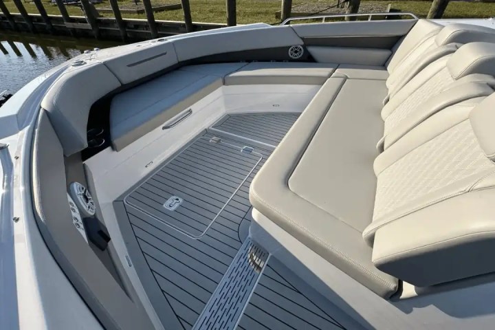 Boat's bow seating area with gray cushioned seats and speakers by the water.