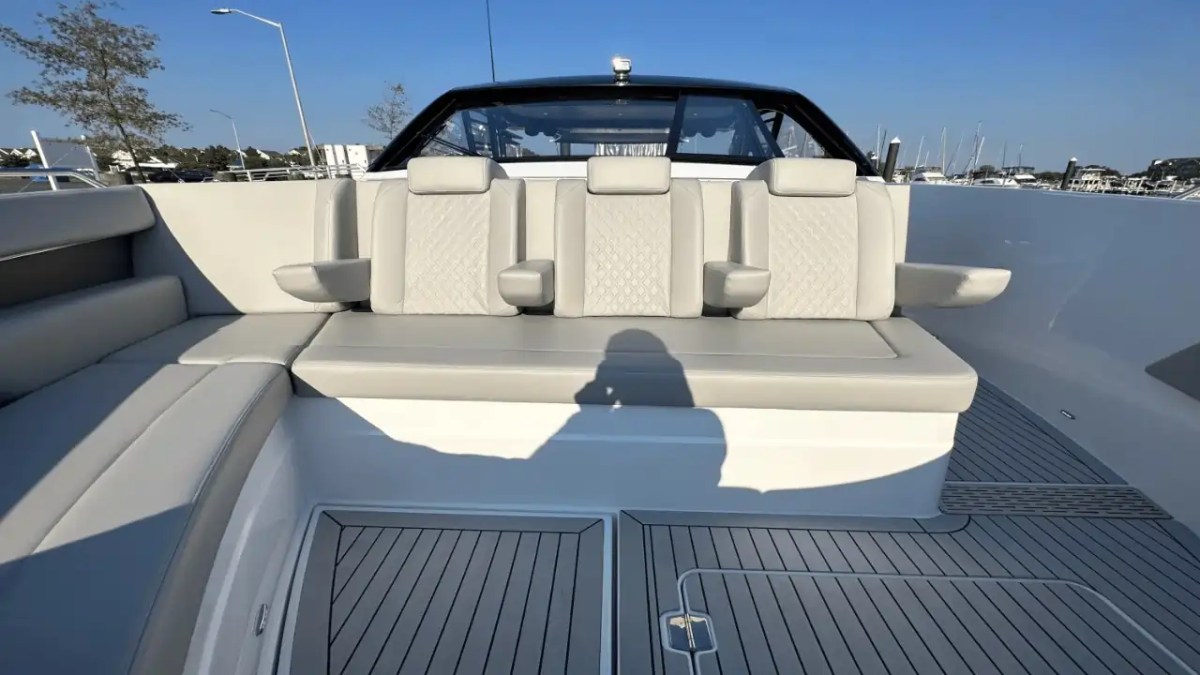 Boat seating area with beige cushioned seats and armrests, wooden deck visible.