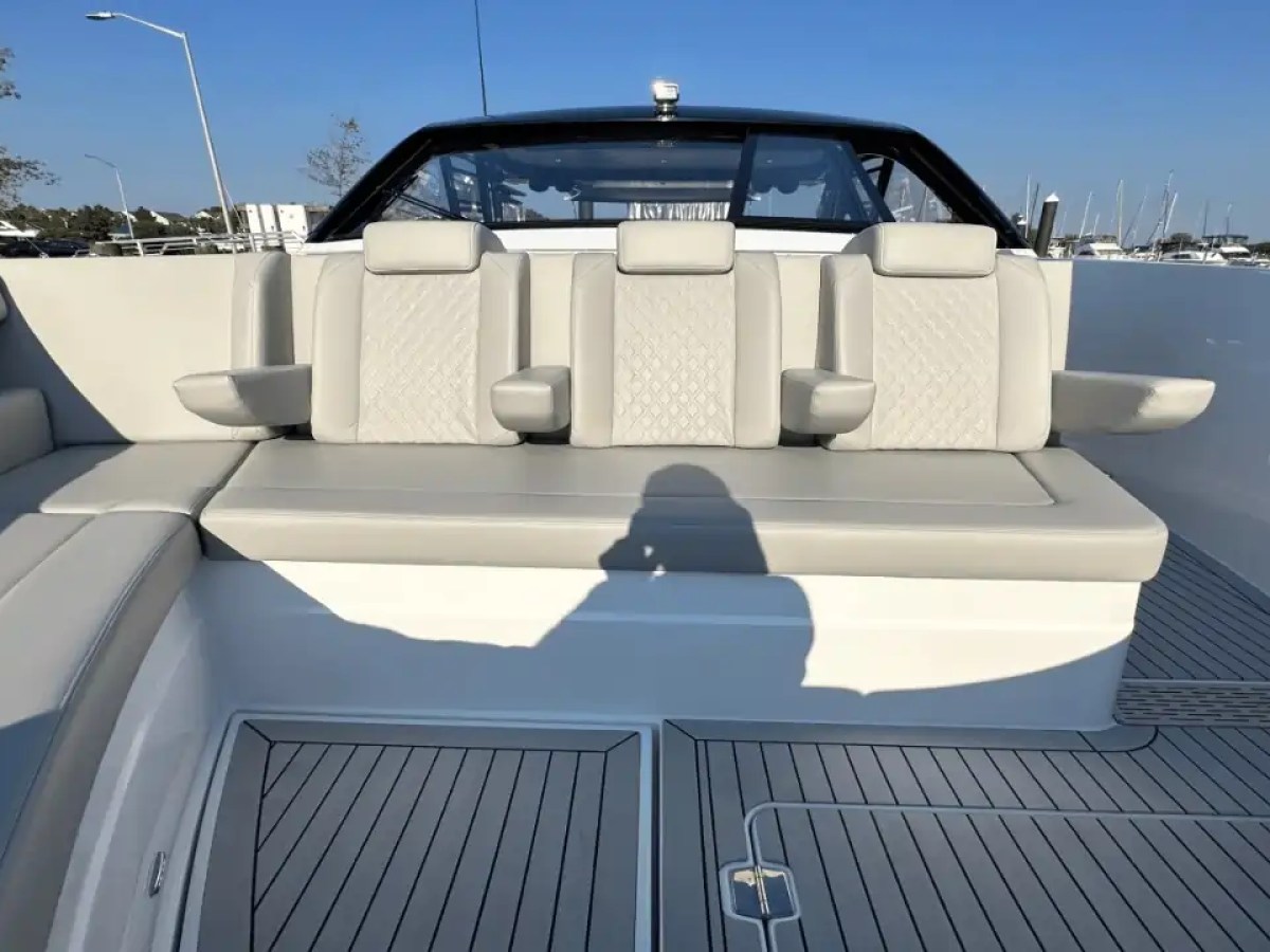 Boat seating area with beige cushioned seats and armrests, wooden deck visible.