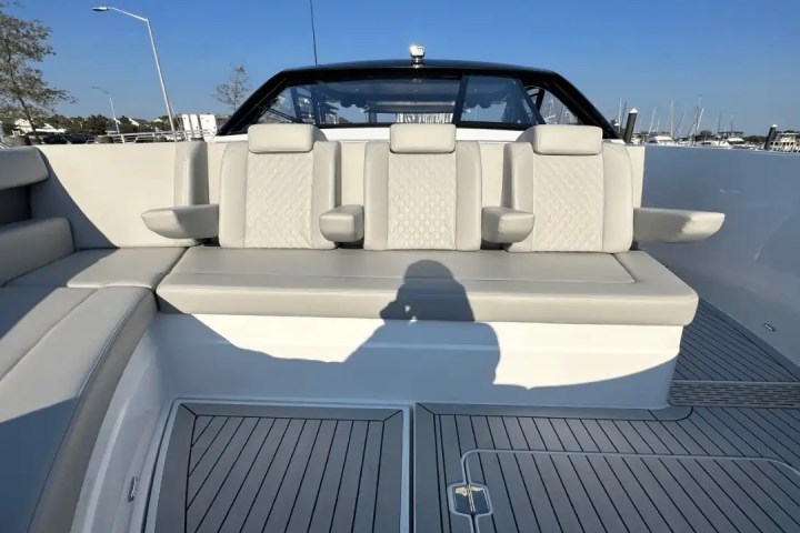 Boat seating area with beige cushioned seats and armrests, wooden deck visible.