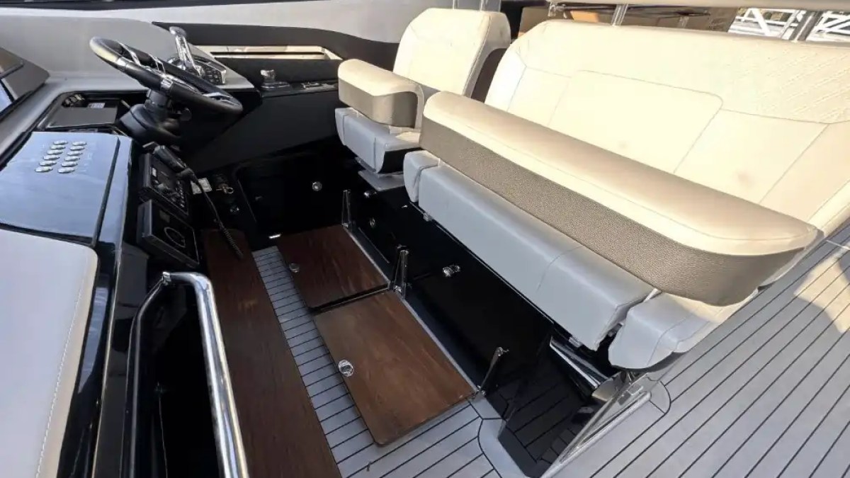 Boat cockpit with steering wheel, controls, and beige padded seats.