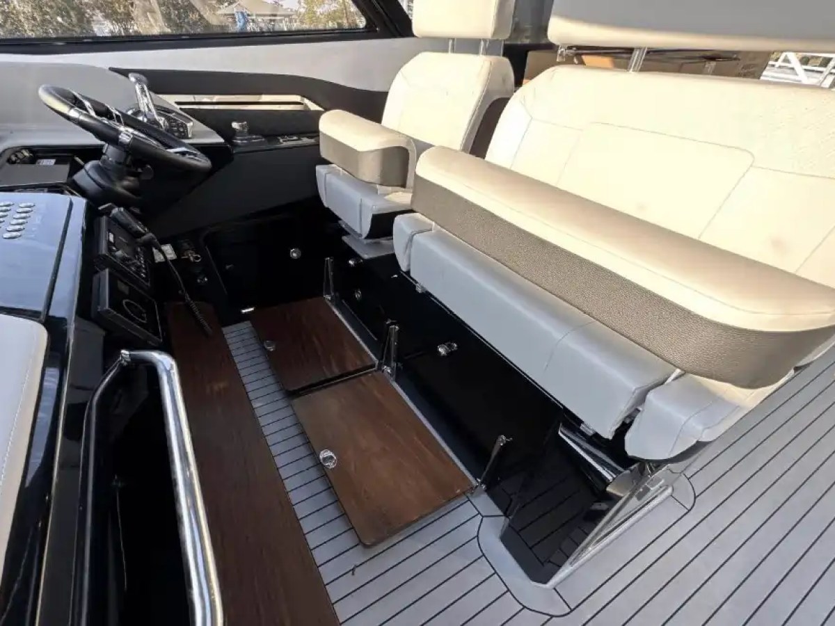Boat cockpit with steering wheel, controls, and beige padded seats.