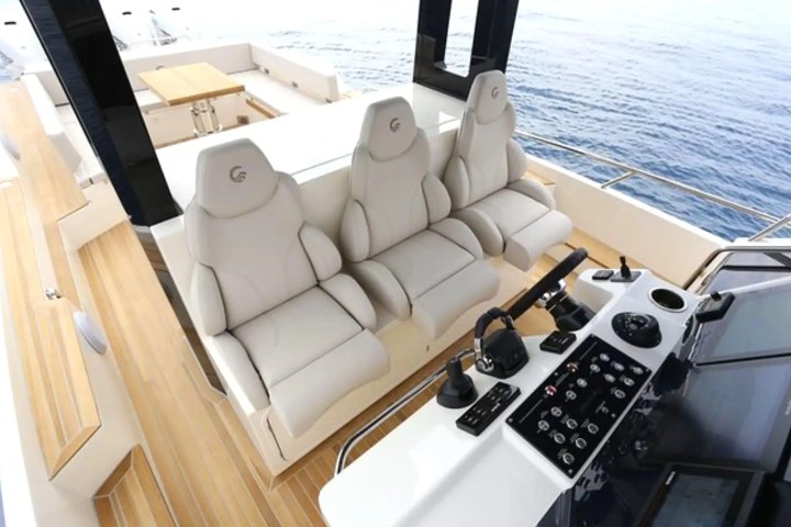 Luxury boat cockpit with three beige seats and a control panel, overlooking the sea.
