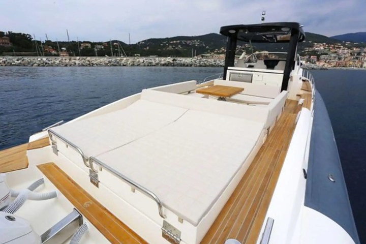 Luxury yacht featuring a sunbathing area and helm, with a coastal town in the background.