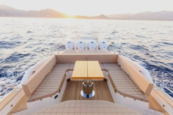 Rear view of a boat with seating and a table, sunset on the ocean horizon.