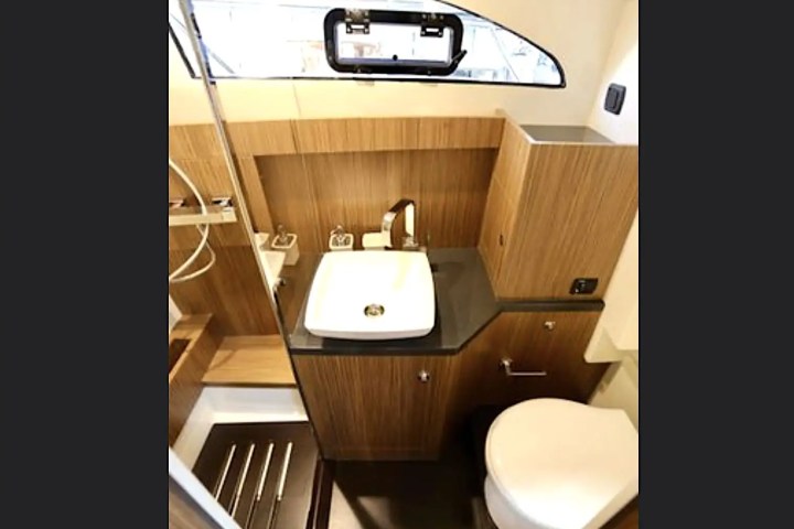 Compact bathroom with a sink, toilet, and wooden cabinetry under a porthole window.