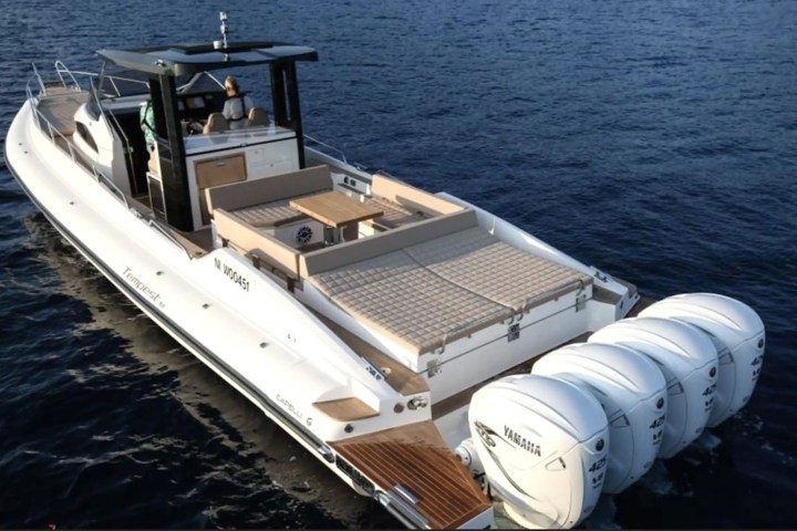A large motorboat with four engines cruising on calm blue water.