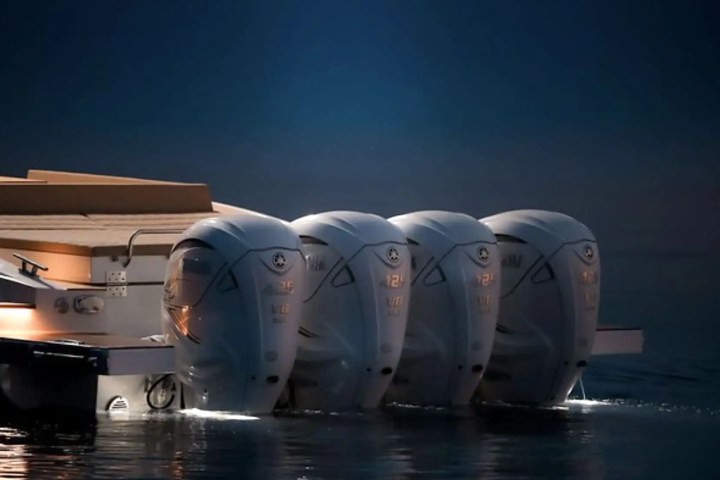 Four boat engines side by side at night, partially submerged in water, with a dark blue sky.
