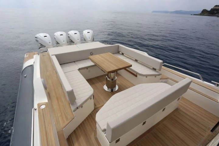 Luxury boat deck with cushioned seating, wooden table, and multiple outboard engines on water.