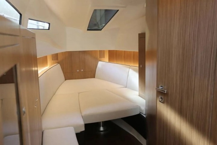 Small boat cabin with white seating and wooden paneling, featuring skylight windows.