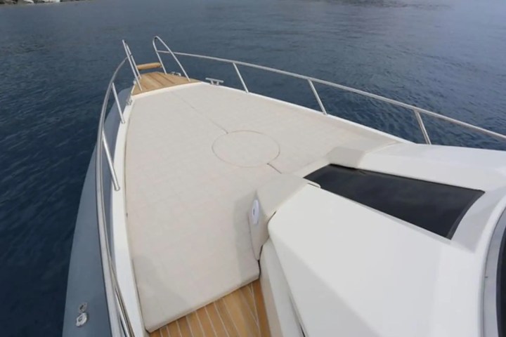 View from the bow of a yacht with a white deck and metal railings, surrounded by calm blue water.