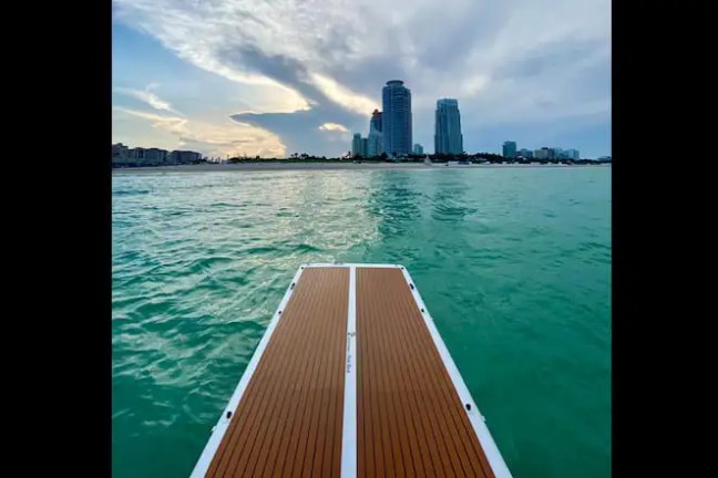 Dock extending over water toward city skyline under cloudy sky.