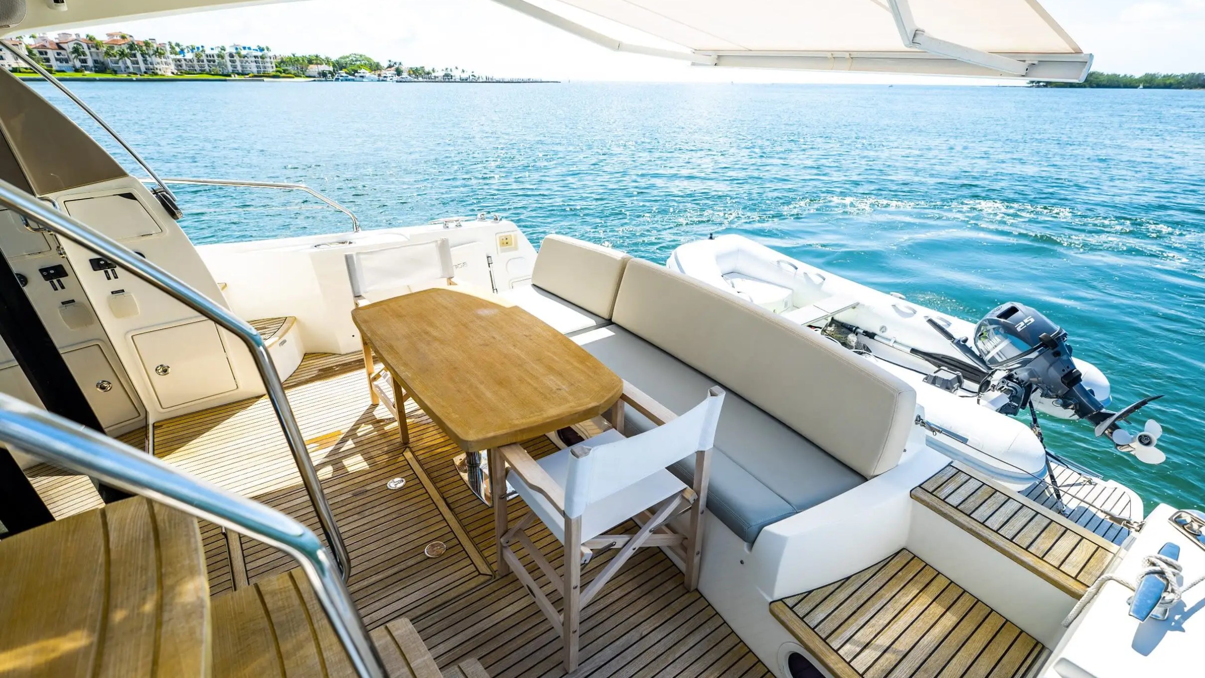 View of a yacht deck with table, chairs, and sea in the background under a sunny sky.