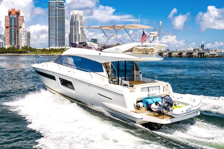Luxury yacht cruising near skyscrapers under a sunny blue sky.