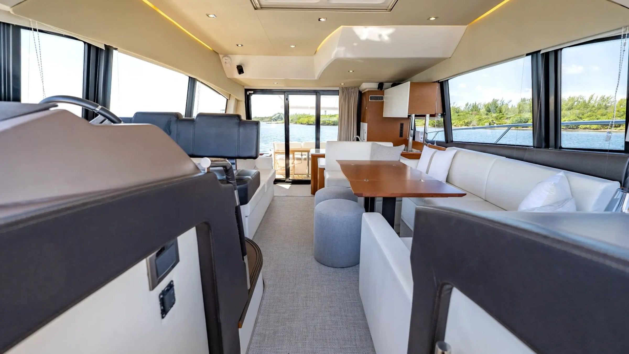 Luxurious yacht interior with white seating, dining table, and large windows overlooking water.