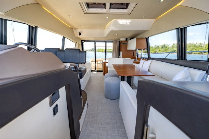 Luxurious yacht interior with white seating, dining table, and large windows overlooking water.