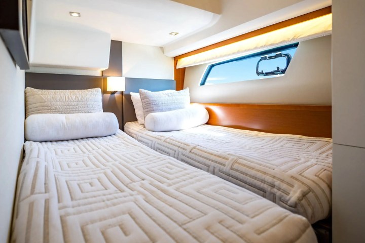 Two twin beds with patterned bedding on a yacht, under a window and accent lighting.
