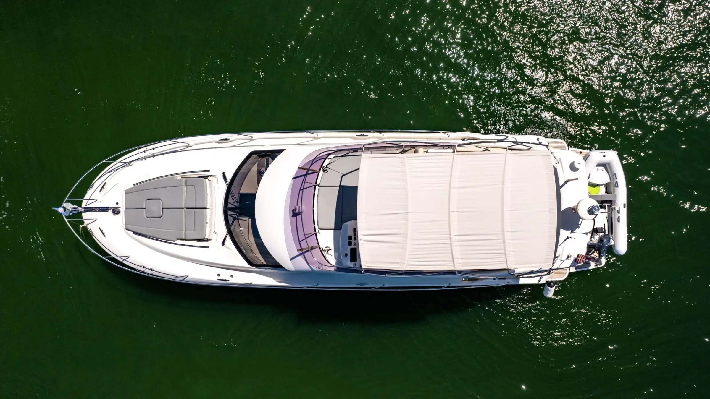 Aerial view of a white yacht with a beige canopy on calm green water.