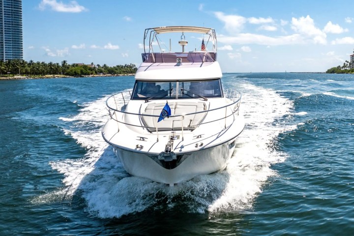 White yacht cruising on blue water, cityscape visible in background under blue sky.