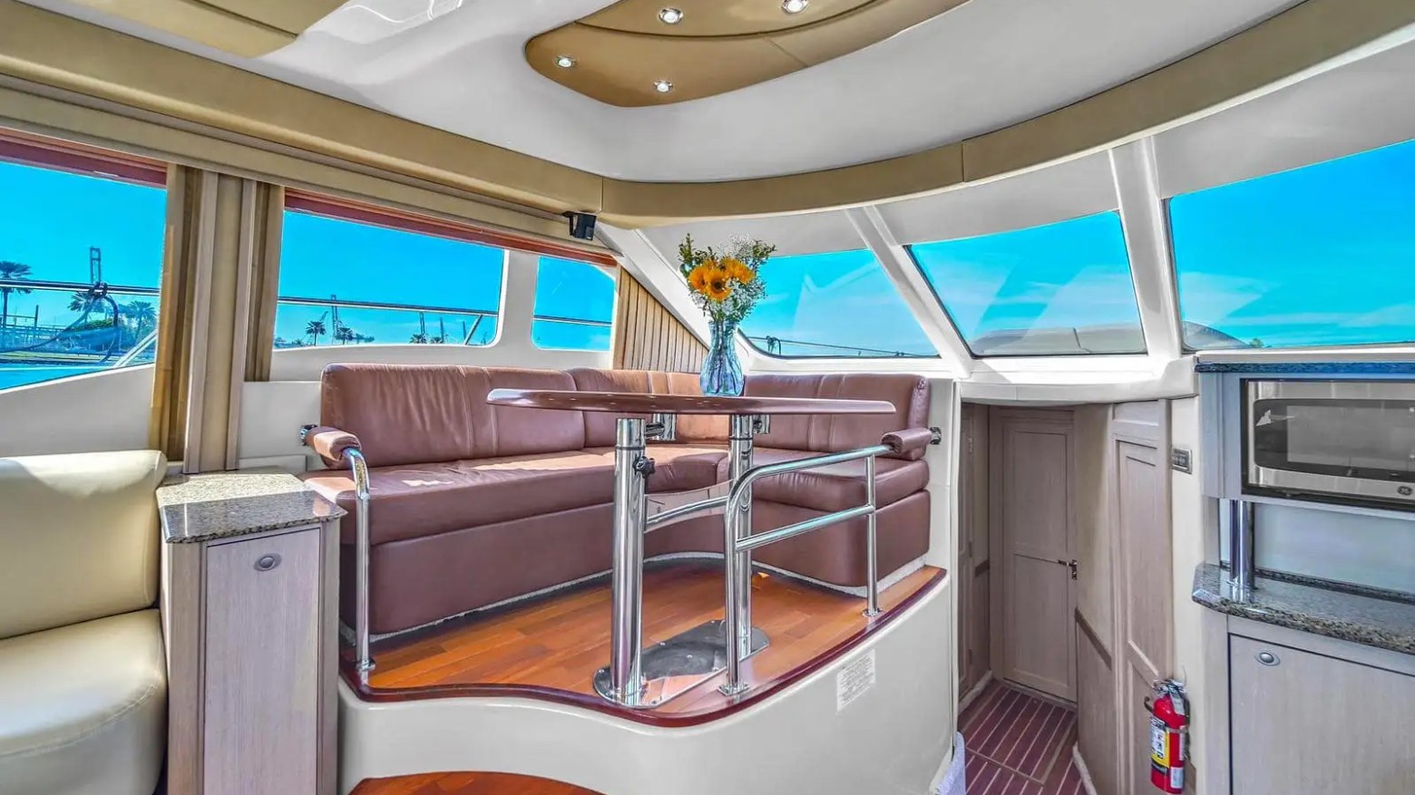 Luxurious yacht interior with leather seating, skylights, and a vase of flowers on a polished wooden floor.