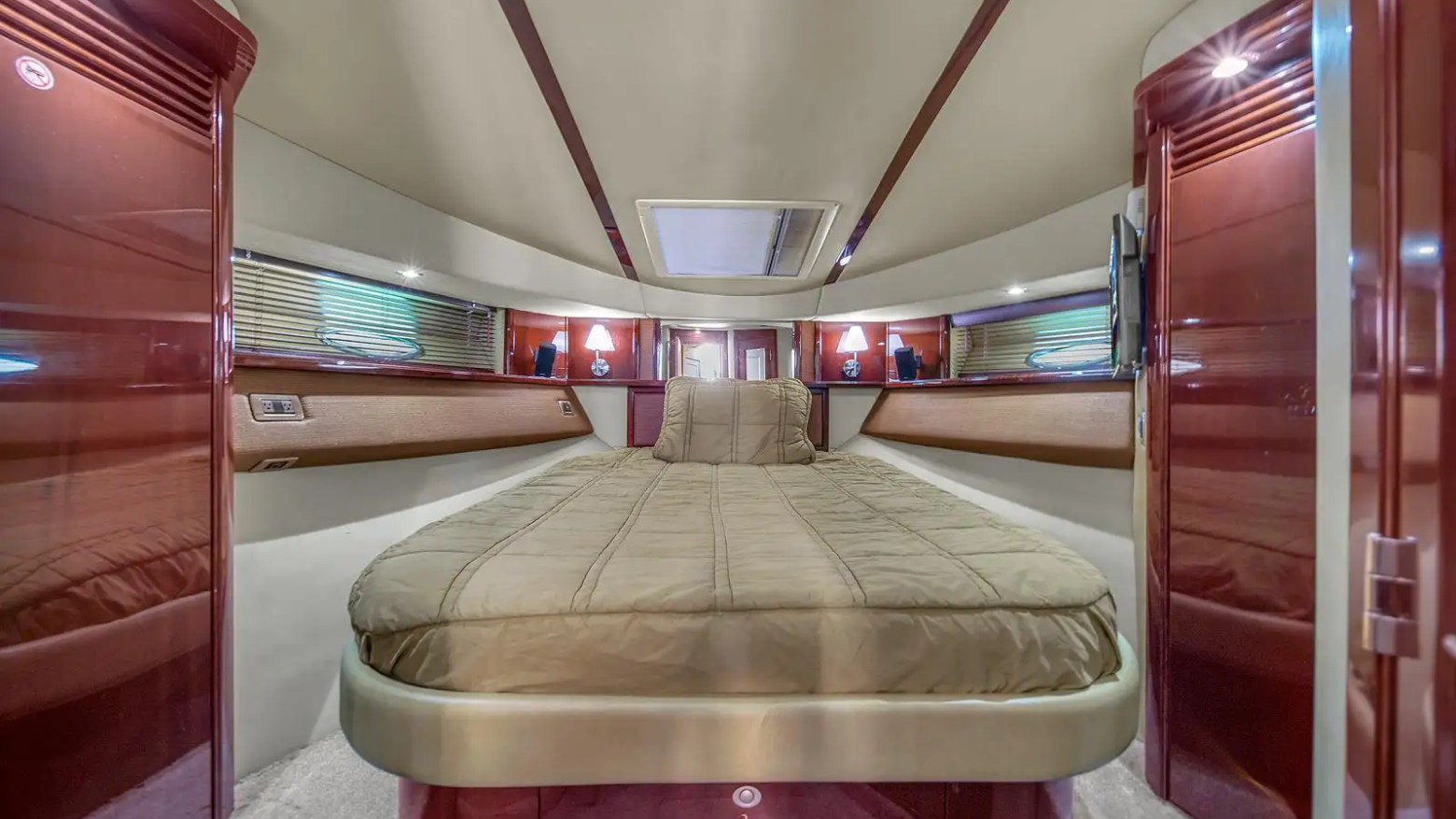 Interior of a yacht cabin with a bed, wood paneling, and small windows on either side.