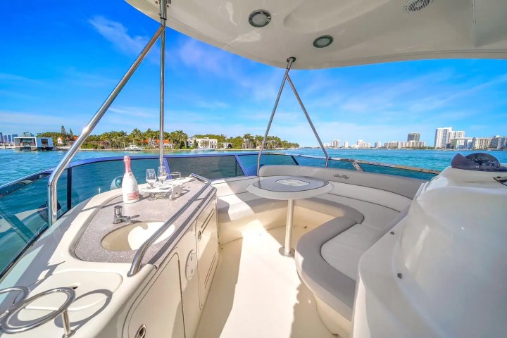 Luxury boat deck with seating, table, and champagne bottle on a sunny day overlooking a coastal city view.
