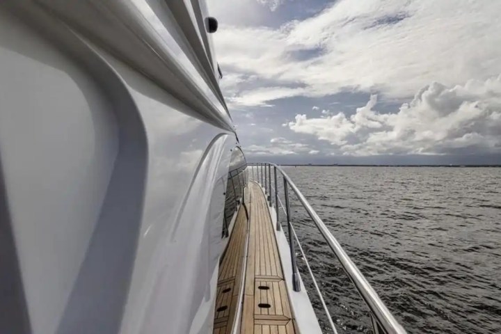 Side view of yacht deck with railing, cloudy sky, and calm ocean.
