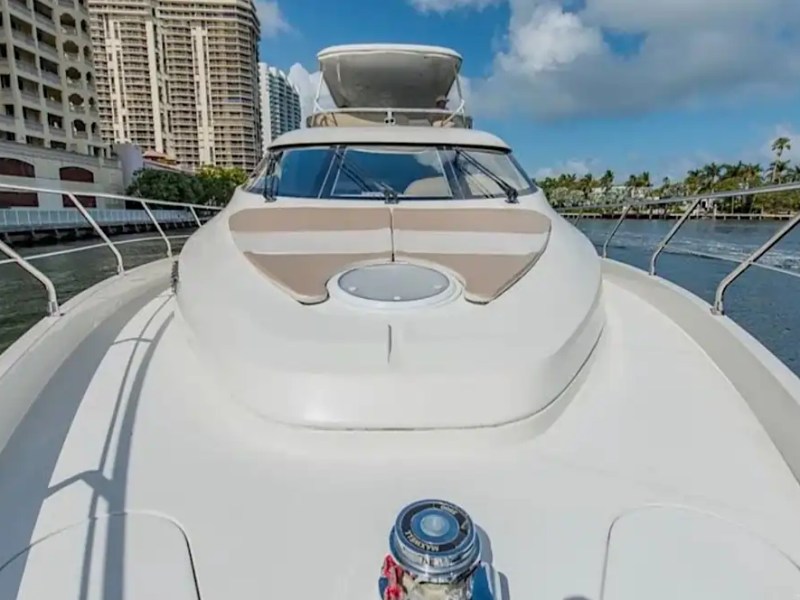 Close-up of a yacht's bow on water with buildings and trees in the background.