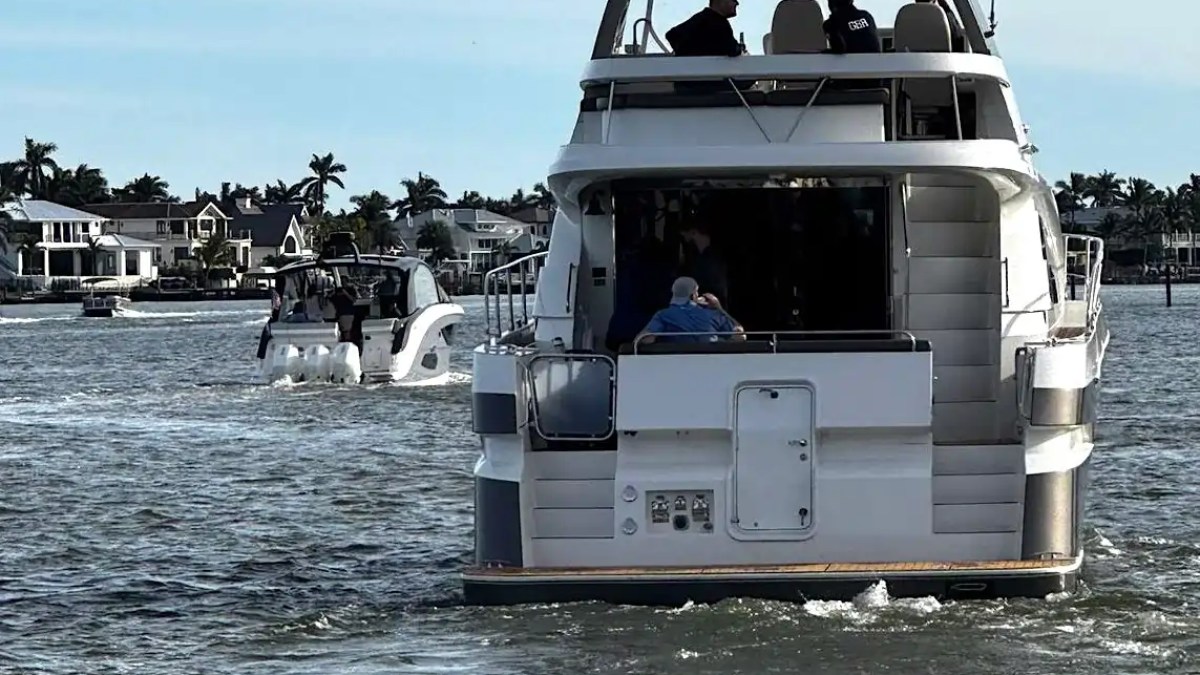 Two boats on the water near a residential area with palm trees in the background.