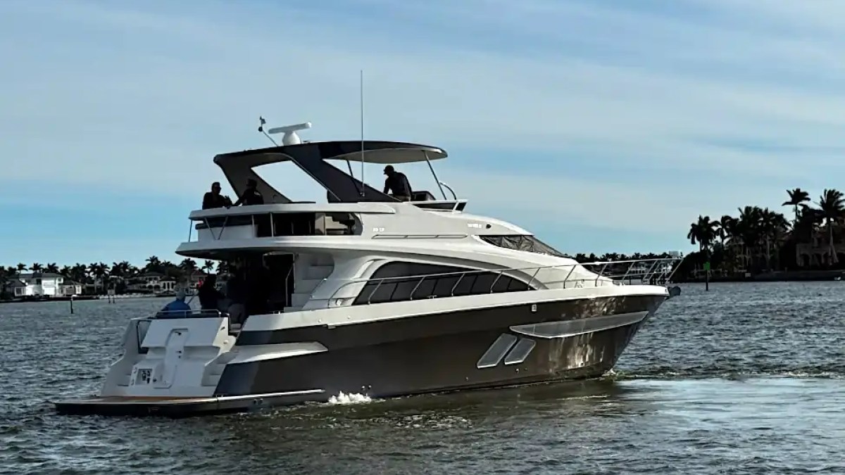 Modern yacht with people on deck cruising in a calm coastal area.