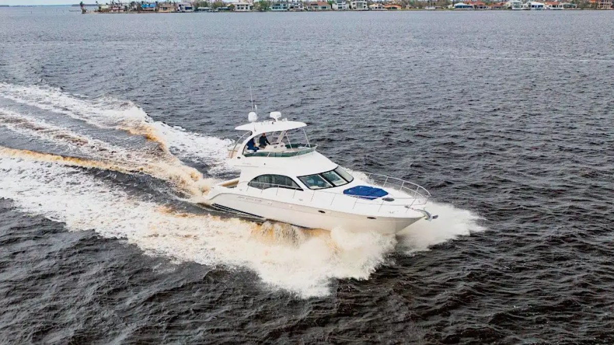 White yacht cruising on open water with shoreline in the background.