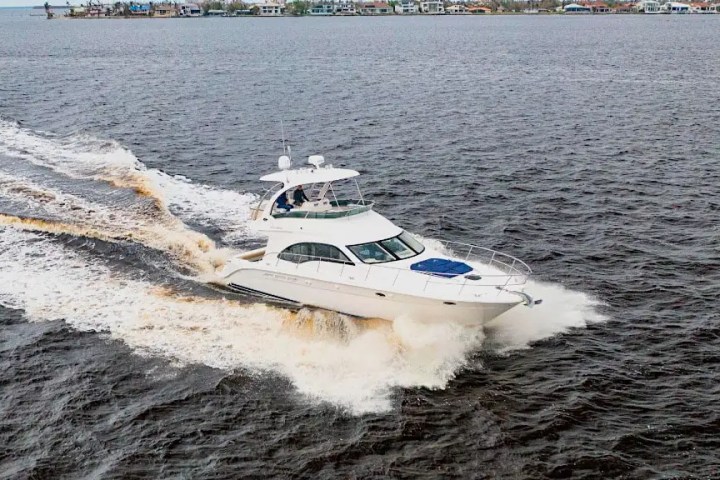 White yacht cruising on open water with shoreline in the background.