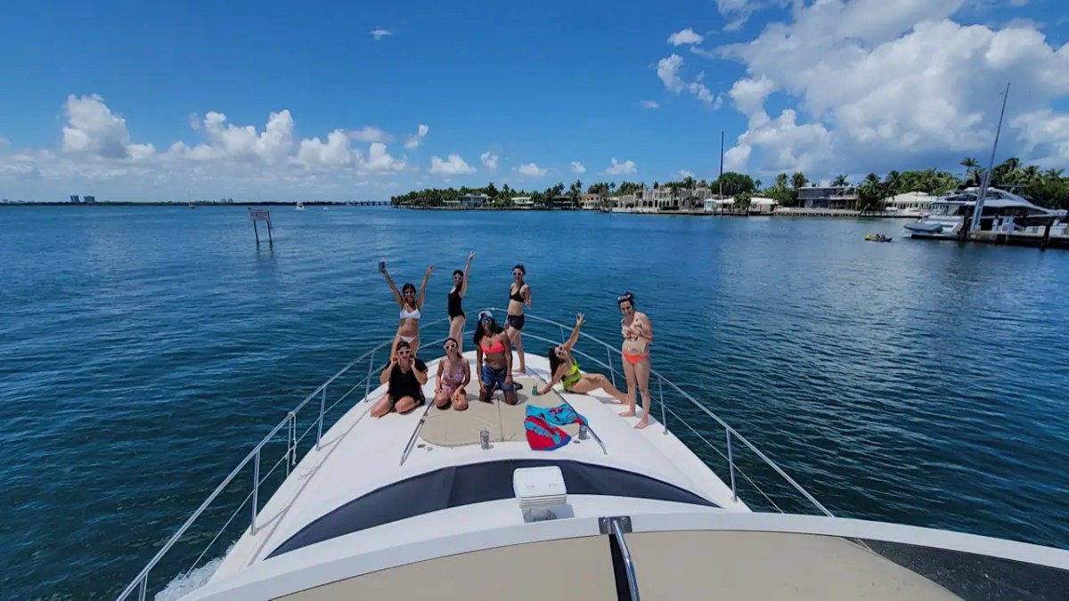 A group of people in swimsuits on a yacht, with clear blue sky and water in the background.