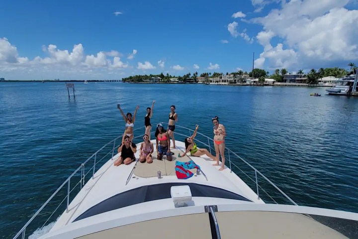 A group of people in swimsuits on a yacht, with clear blue sky and water in the background.