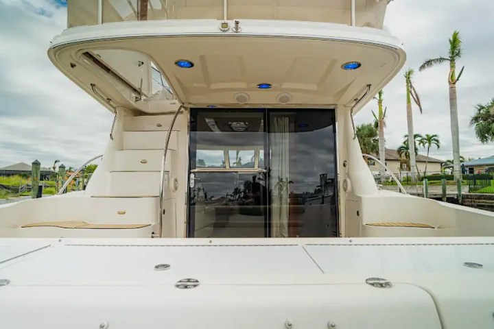 View of a yacht's back with stairs and outdoor seating on a sunny day.
