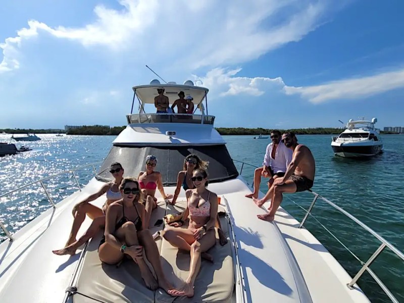 Group of people relaxing on a yacht in sunny weather with other boats nearby.
