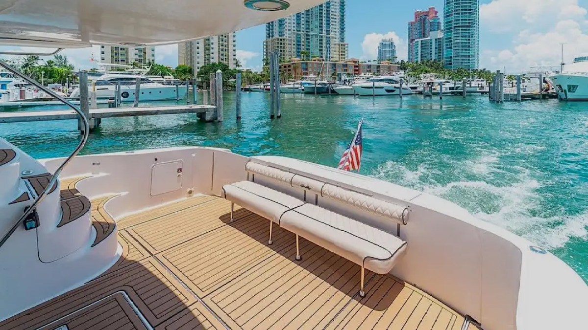 View from yacht deck with seating, American flag, city skyline, and docked boats in the background.