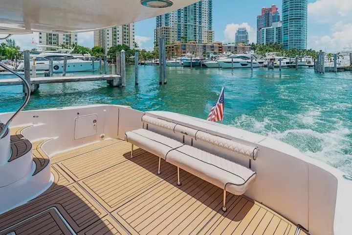 View from yacht deck with seating, American flag, city skyline, and docked boats in the background.