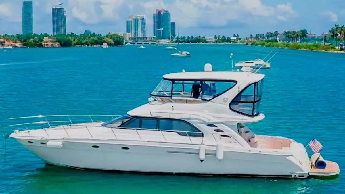 White yacht with two decks on blue water, city skyline in background.