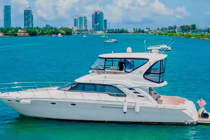 White yacht with two decks on blue water, city skyline in background.