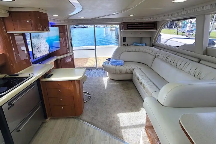 Interior of a yacht showing a modern kitchen, white sofa, and large windows with a water view.